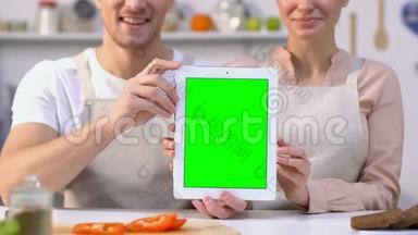 穿着围裙，手里拿着绿色屏幕平板<strong>电脑</strong>坐在厨房<strong>收据</strong>上的一对快乐的夫妇